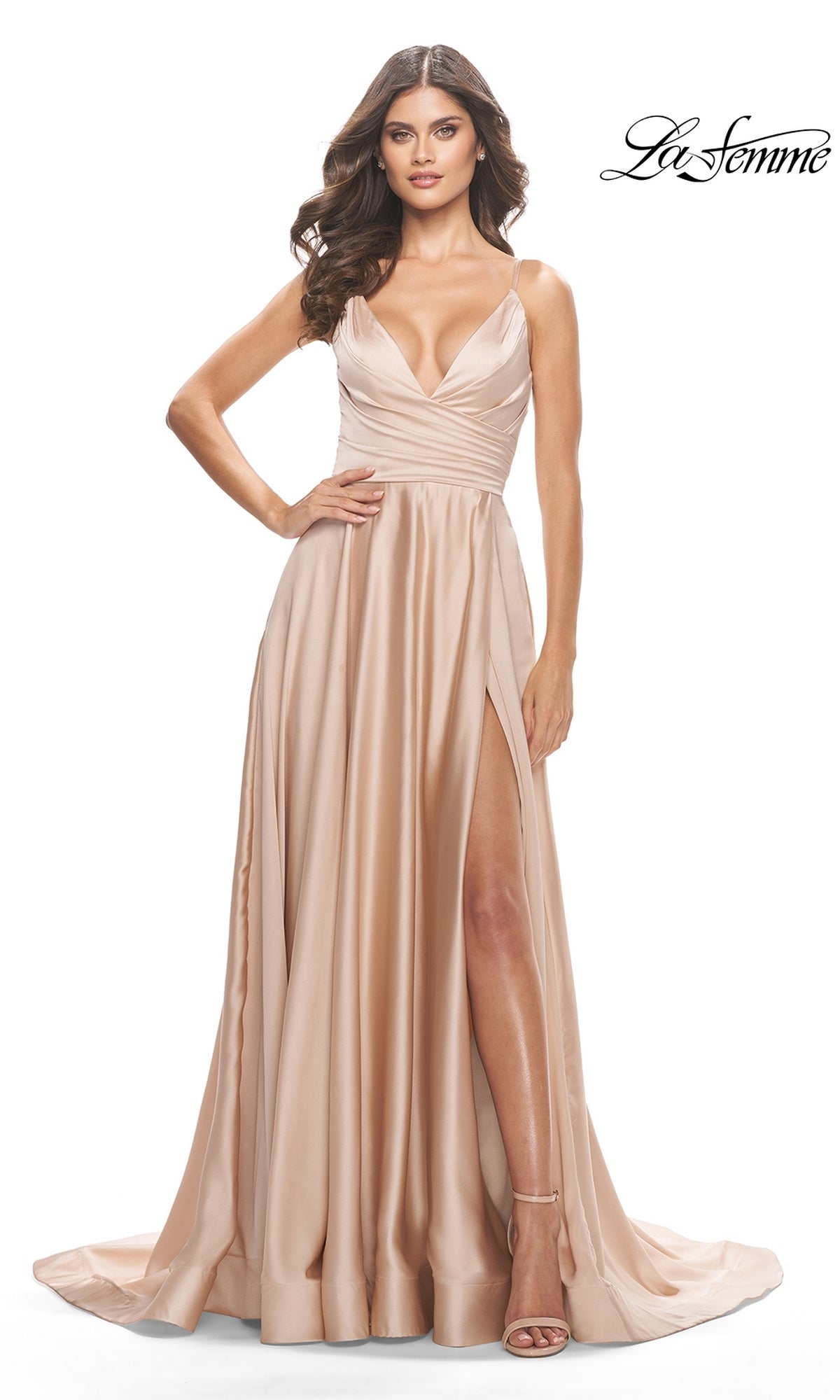 A woman poses in the La Femme V-Neck Long A-Line Prom Dress 31505, a floor-length champagne satin gown with a deep neckline, ruched bodice, thin straps, and high slit, elegantly set against a white background.